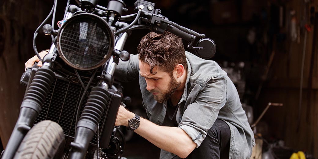 Mann kniet vor seinem Motorrad und repariert es