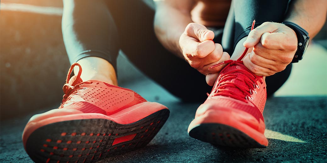 Mann sitzt auf dem Boden und schnürt sich seine roten Laufschuhe