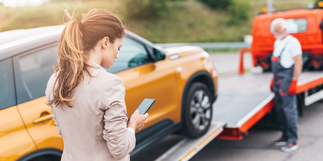 Eine Frau schaut auf ihr Smartphone, während ihr Auto abgeschleppt wird.